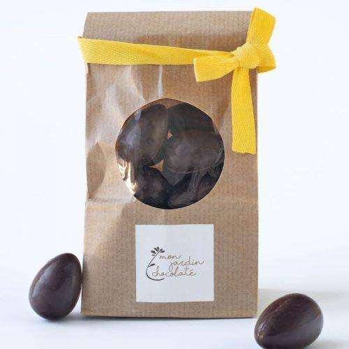 sachet avec un ruban jaune, rempli d'oeufs au chocolat noir fourrés avec des noisettes et deux oeufs au chocolat à gauche et à droite
