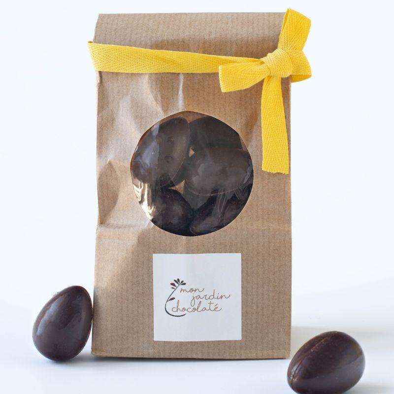 sachet avec un ruban jaune, rempli d'oeufs au chocolat noir fourrés avec des noisettes et deux oeufs au chocolat à gauche et à droite