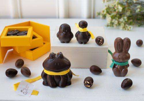 figurines grenouille, lapin, pingouin et oeufs en chocolat de pâques avec une boîte de 12 pralinés ouverte à gauche