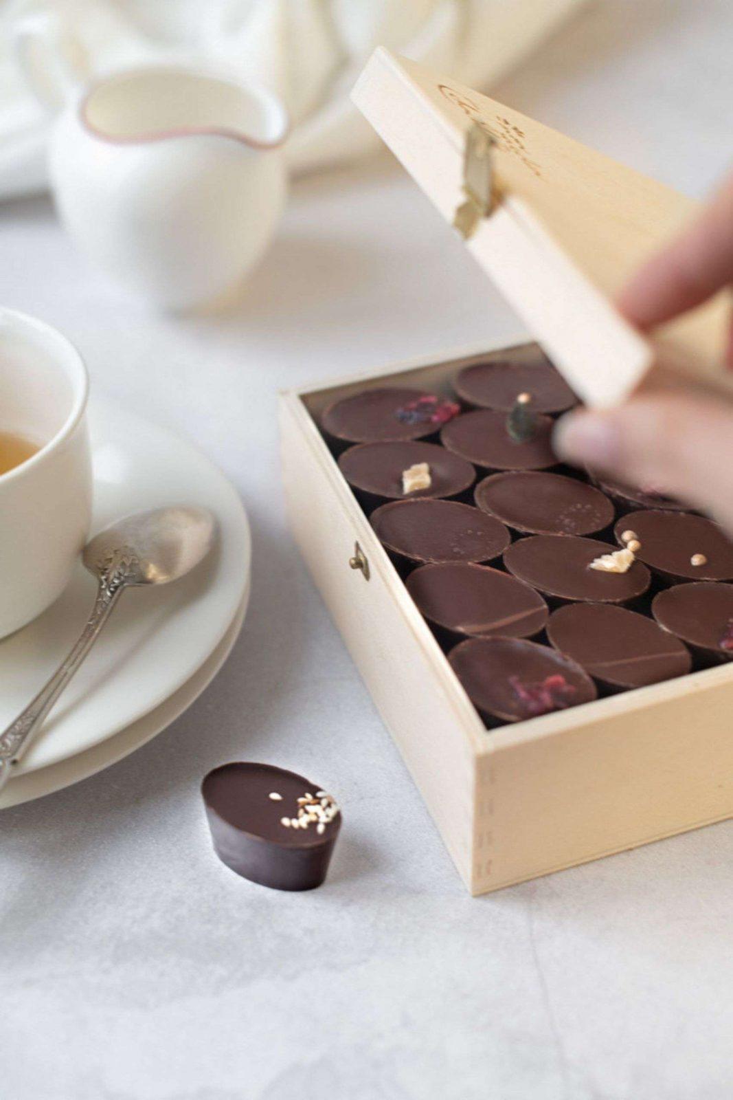 boîte en bois remplis de chocolats individuels à droite et une tasse de thé sur une petite assiette à gauche